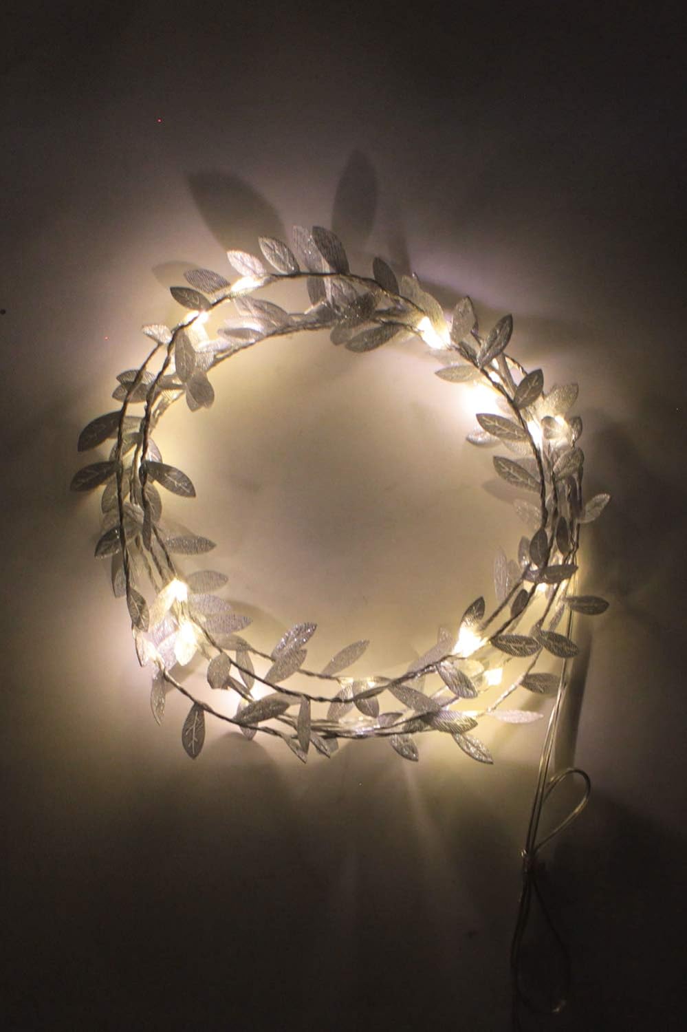 Silberne Lichterranke mit Blättern als Kranz geformt mit leuchtenden LED-Lichtern an dunkler Wand