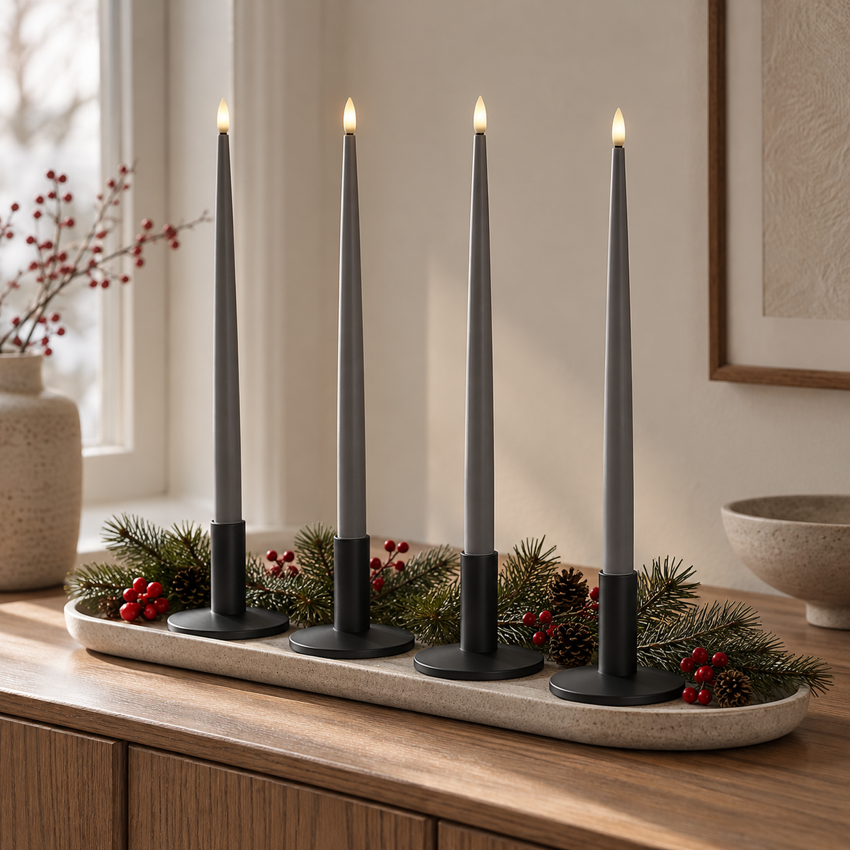 Vier graue LED-Stabkerzen in schwarzen Kerzenhaltern auf einer langen Steinschale mit Tannengrün und roten Beeren auf einem Holz-Sideboard