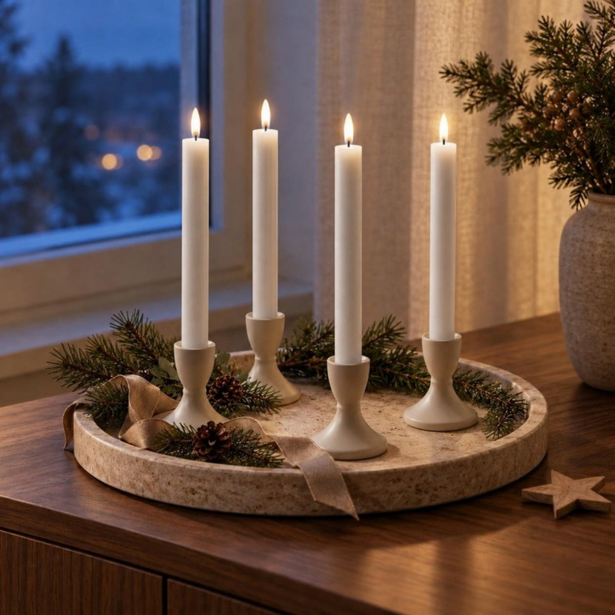 Vier weiße LED-Stabkerzen im Wetlook in Kerzenhaltern auf einem runden Terrazzo-Tablett mit Tannengrün und Band auf einem Sideboard am Winterabend