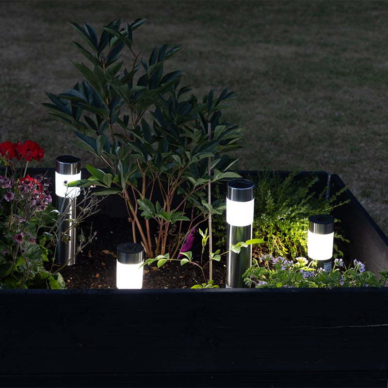 Zwei Solarleuchten aus Stahl mit weißem Licht zwischen Pflanzen im Gartenbeet