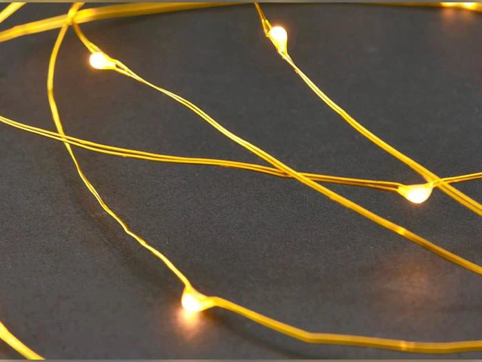Nahaufnahme einer eingeschalteten Lichterkette aus Messing mit kleinen, warmweißen LED-Lämpchen auf dunkelgrauem Hintergrund.