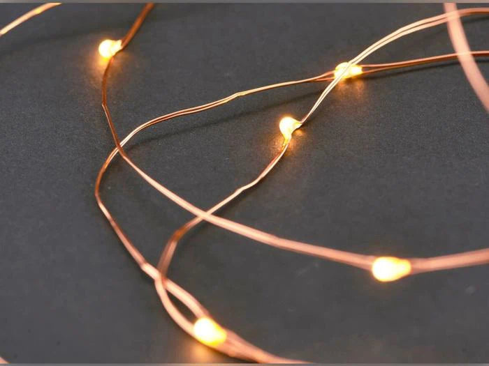 Leuchtende kupferfarbene Lichterkette mit warmweißen LEDs vor dunklem Hintergrund