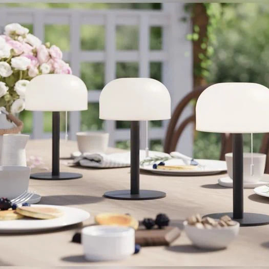 Drei schwarze LED Tischlampen auf gedecktem Gartentisch mit Gebäck, Beeren und Blumen