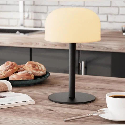 Eingeschaltete LED Tischlampe mit warmem Licht auf Küchentheke mit Kaffee und Zimtschnecken